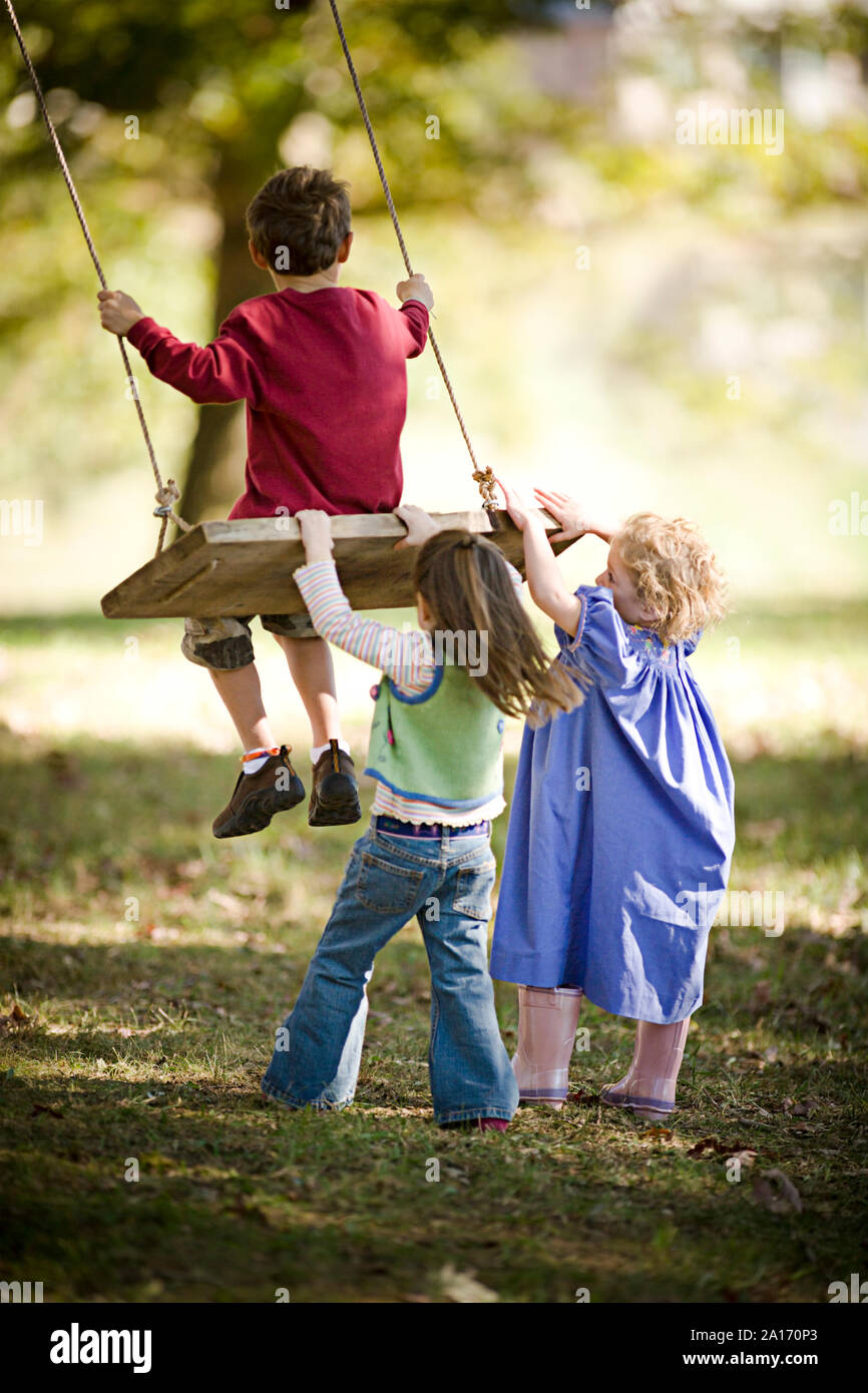 Girls pushing boy on a swing Stock Photo