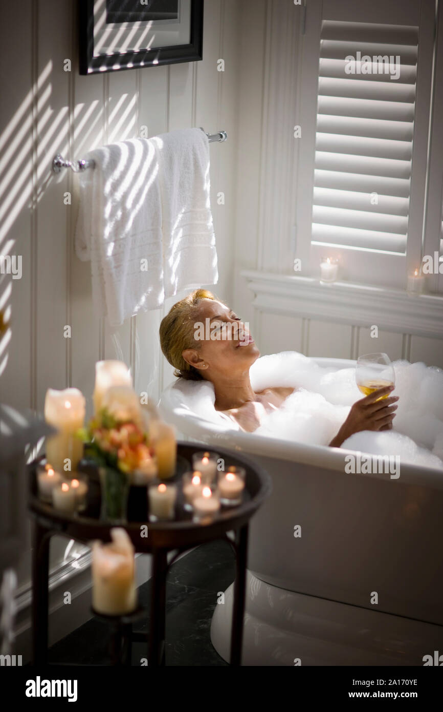 Midadult woman relaxing in a bubble bath with a glass of wine and