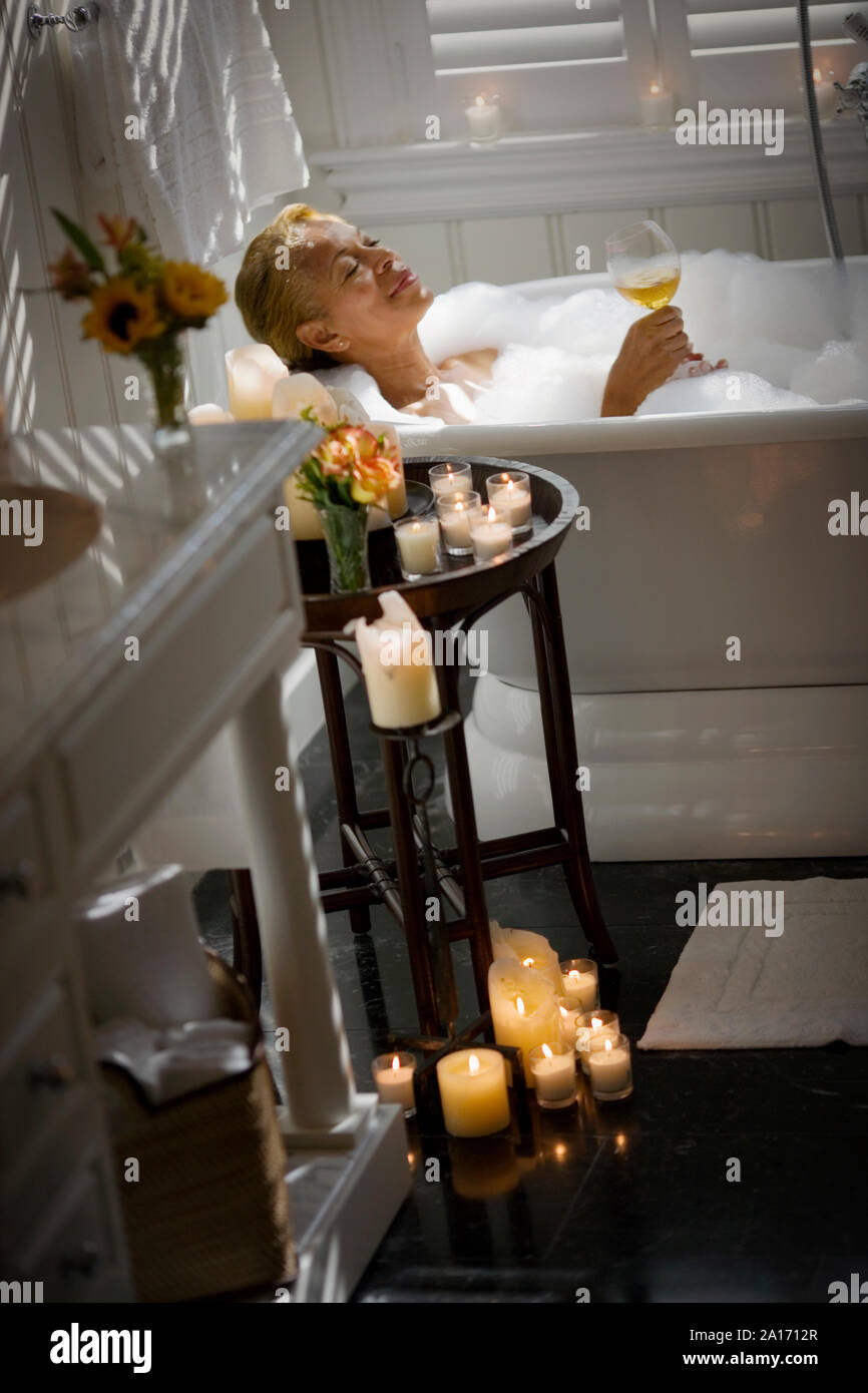 Midadult woman relaxing in a bubble bath with a glass of wine and