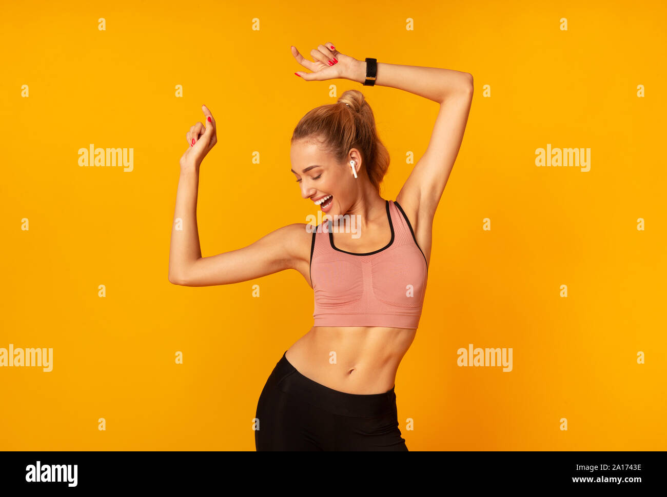 Woman In Wireless Earphones Dancing Listening To Music, Yellow Background Stock Photo
