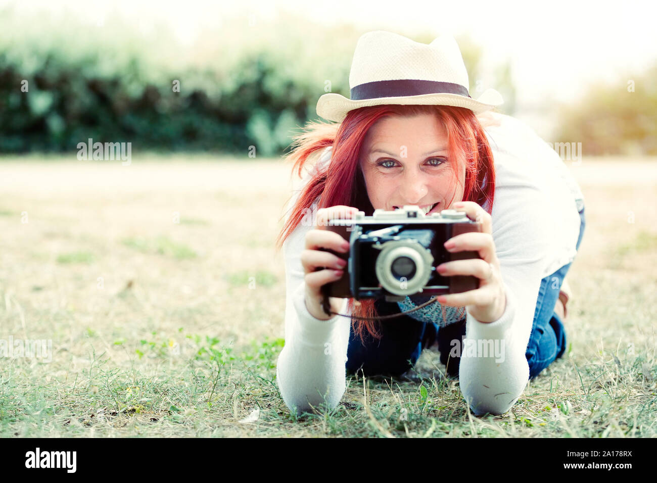 Portrait in the nature of a beautiful smiling red-haired woman using an old camera. vintage treatment Stock Photo