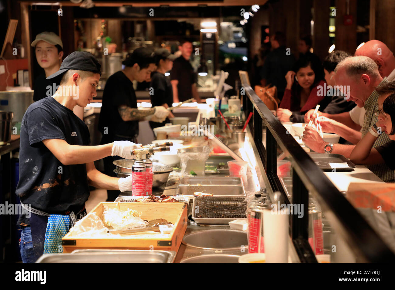 Cooks working in the open kitchen of Mr.Taka Ramen Japanese Soup Bowls with customers in Time Out Market New York in DUMBO Brooklyn.New York City.USA Stock Photo
