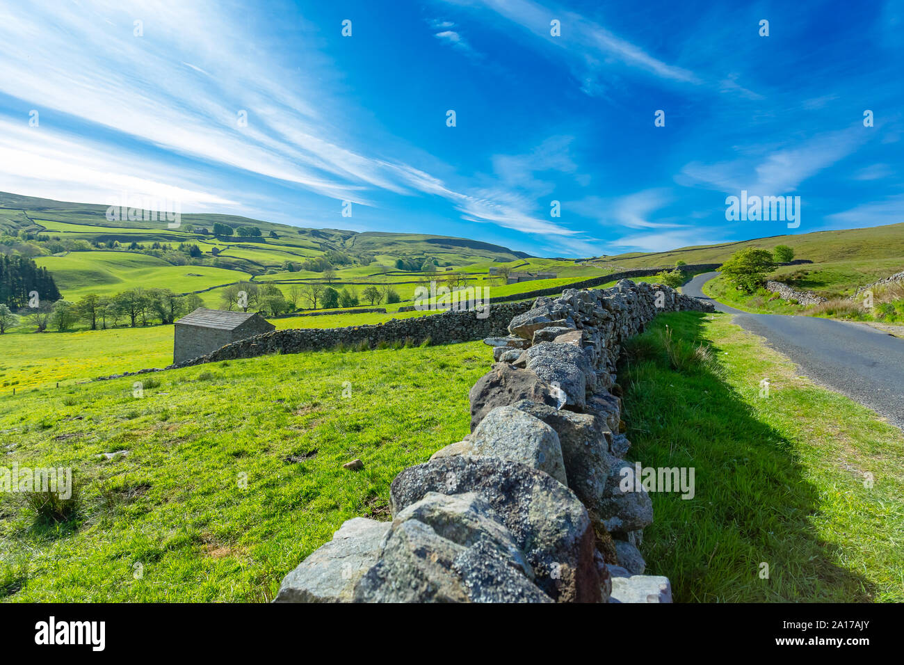 Yorkshire Dales scenic landscape.  Single track road from Askrigg to Gunnerside and Muker.  Blue sky, drystone walling and green fields. Landscape Stock Photo