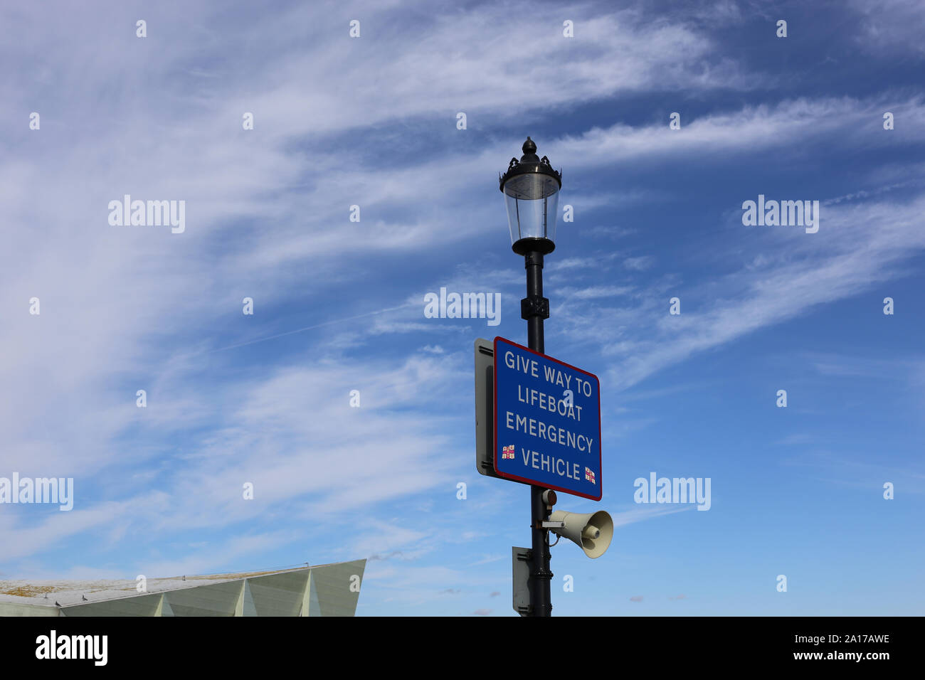 A sign stating 'Give Way to Lifeboat Emergency Vehicle', with a blue sky and cloud background, at the end of Southend Pier. Stock Photo
