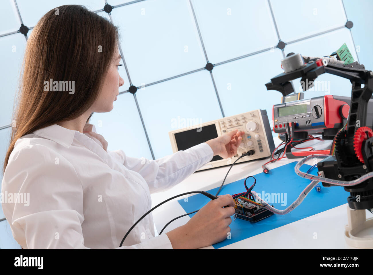 A young woman writes an algorithm for the robot arm. Science Research Laboratory for Robotic Arm Model. Computer Laboratory Stock Photo