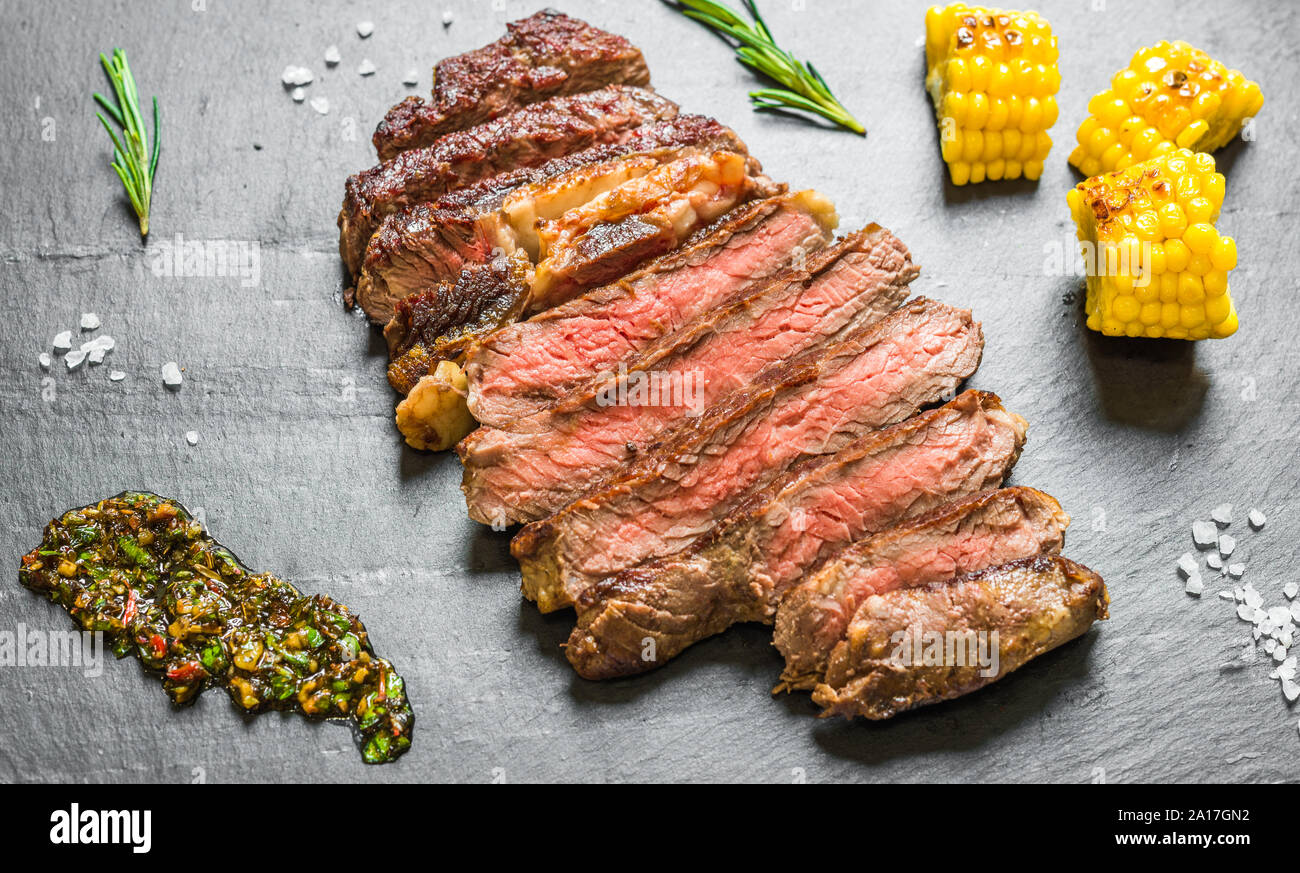 Sliced medium rib eye beef steak meat with chimichurri on black ...