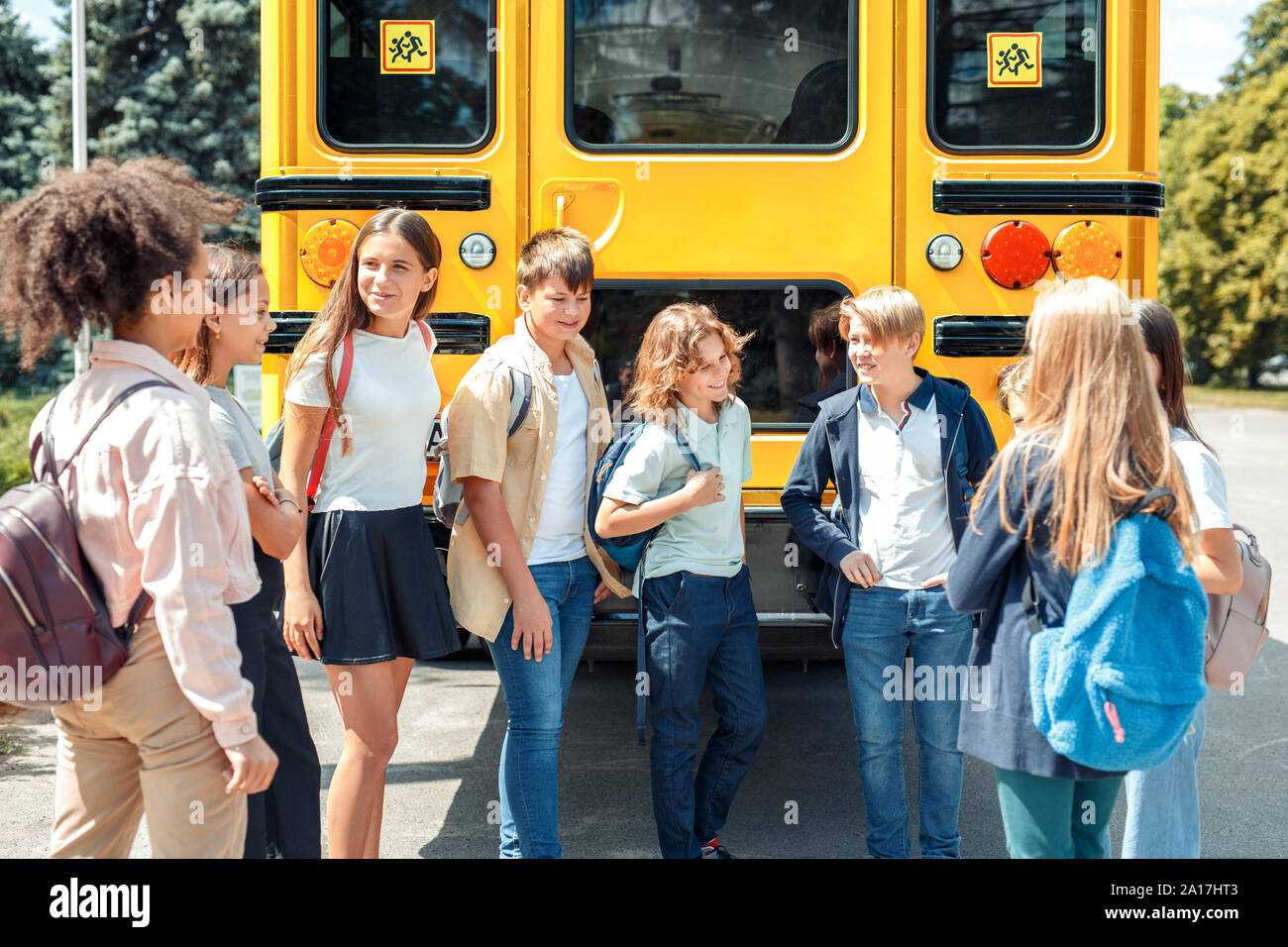 Classmates going to school standing near bus talking happy Stock Photo