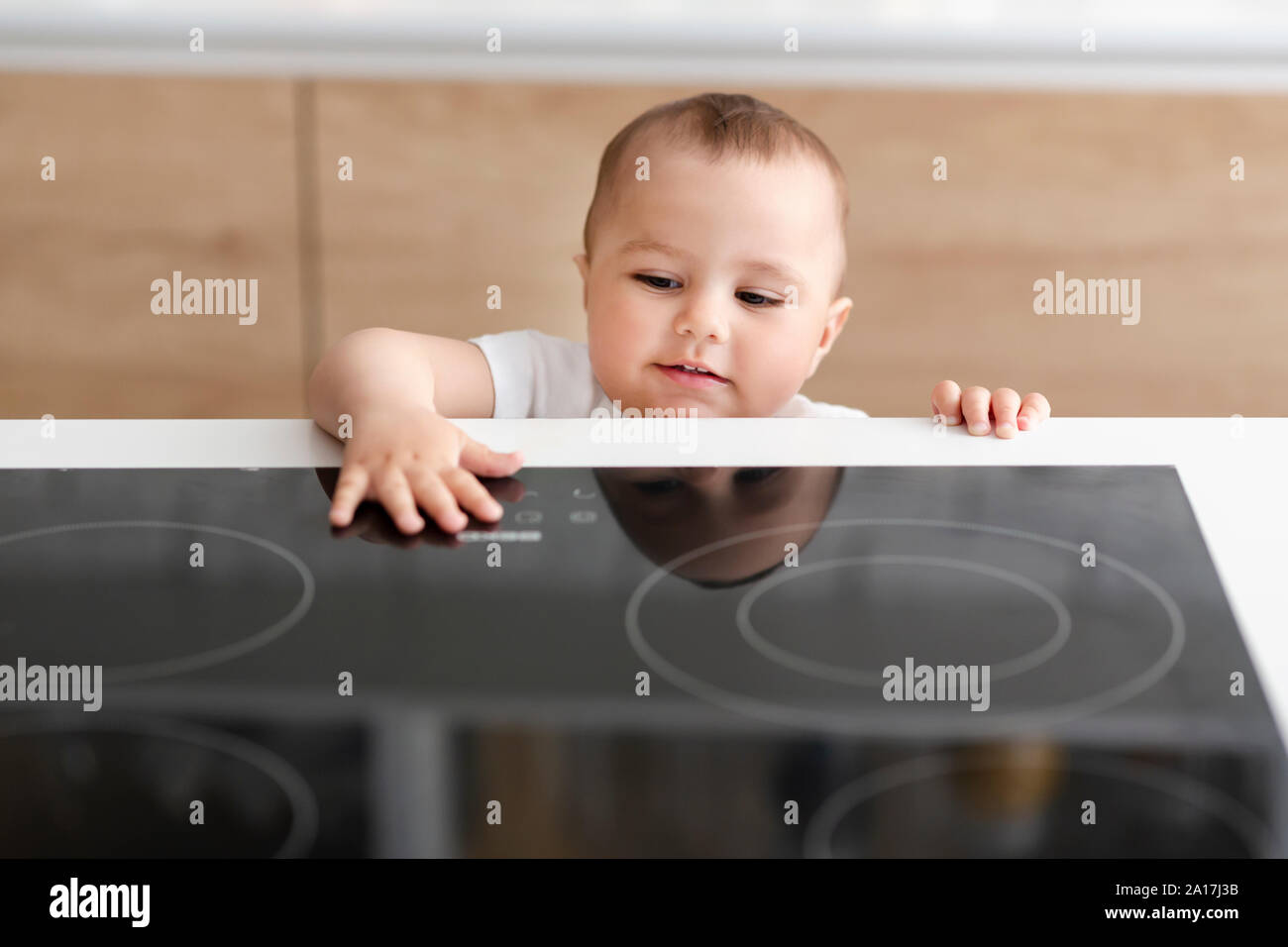 Curious toddler reaching hand to hot electric cooktop Stock Photo