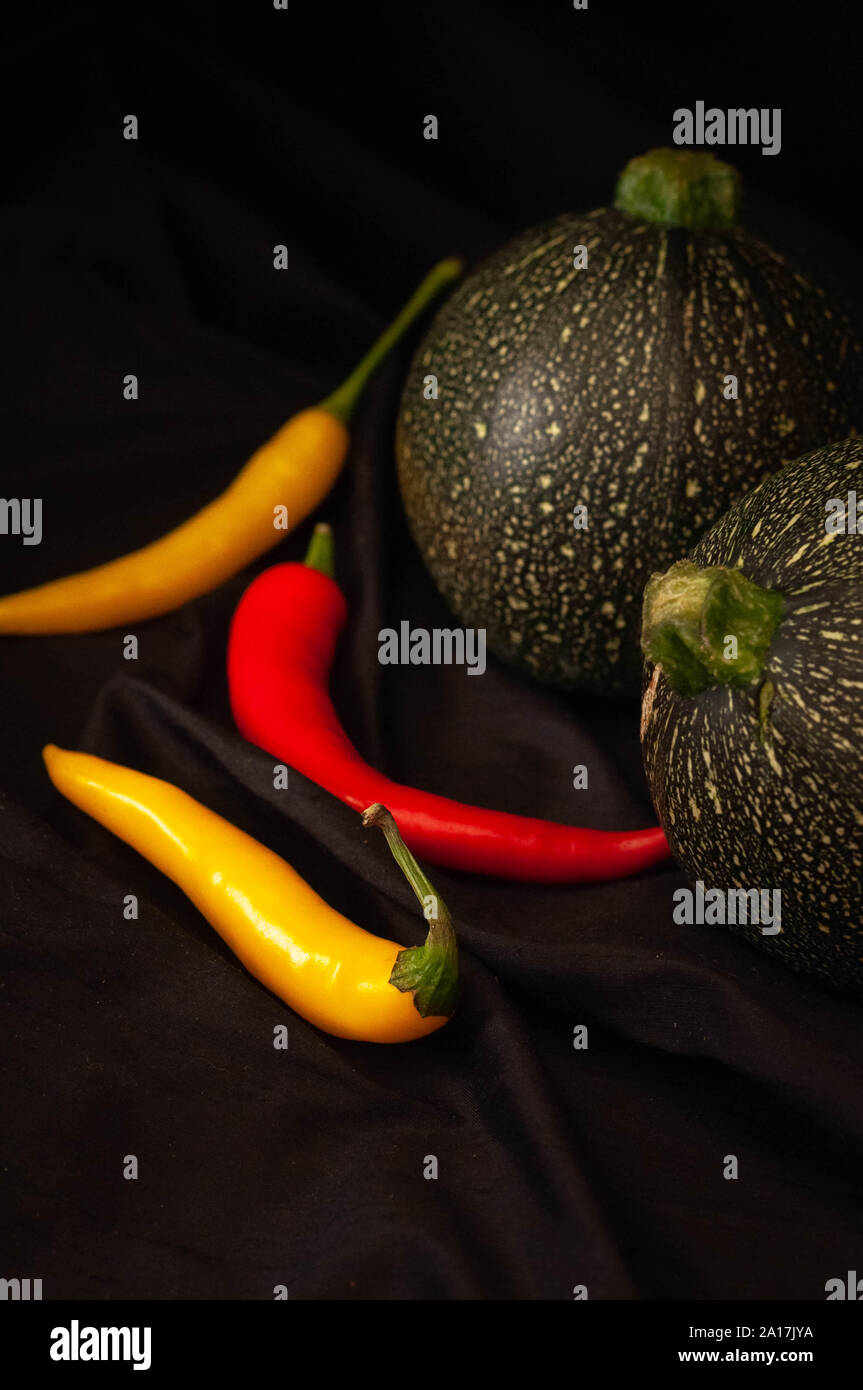 round courgettes and bright hot peppers on a black background Stock Photo