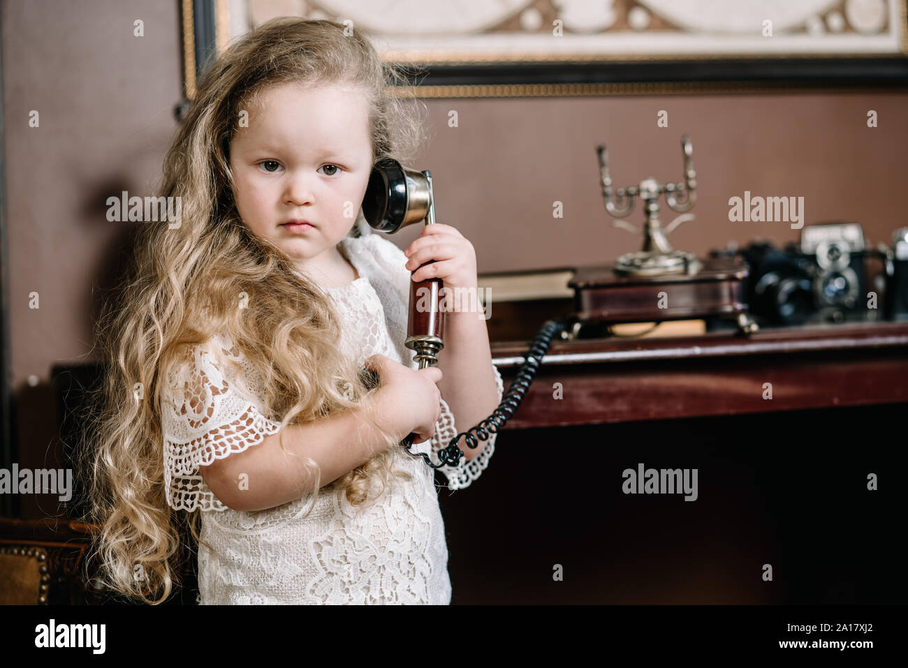 Little brooding child girl talking on a retro telephone in the room ...