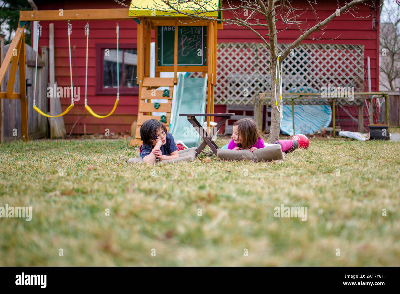 Two happy children lay on mats in their yard chatting together Stock Photo