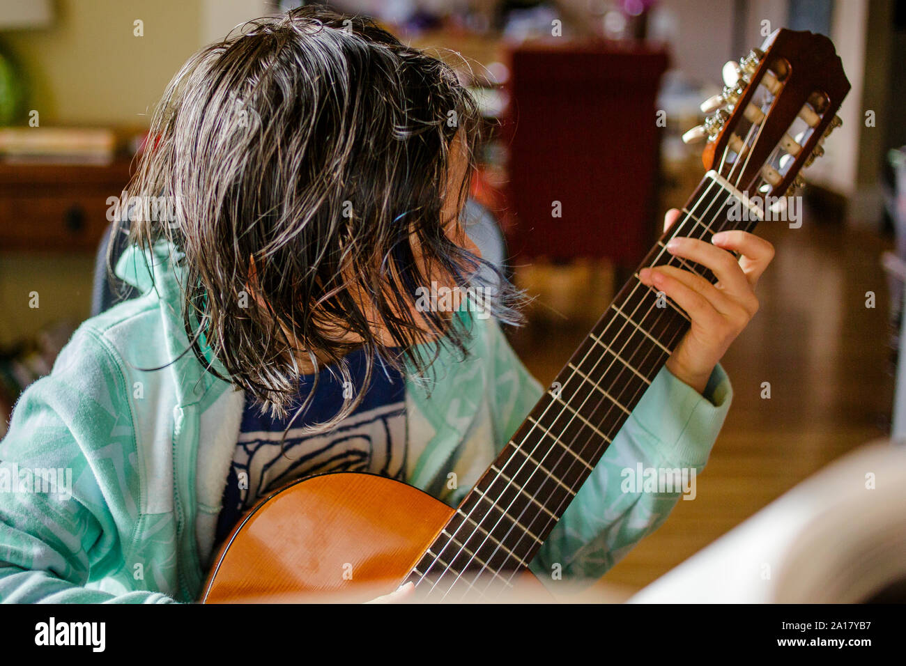 A child with hair hanging  in his face practices classical guitar Stock Photo