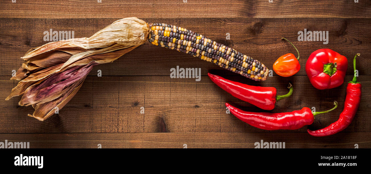 Dried multicolored corn cob with an assortment of fresh peppers on a dark wood background Stock Photo