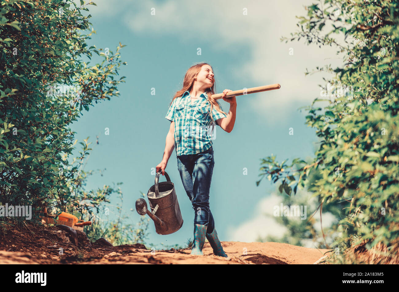 Gardening tips. Spring gardening. Girl child hold shovel watering can. Spring gardening checklist. Little helper. Watering tools that will solve dry yard problems. Gardening guide for beginners. Stock Photo