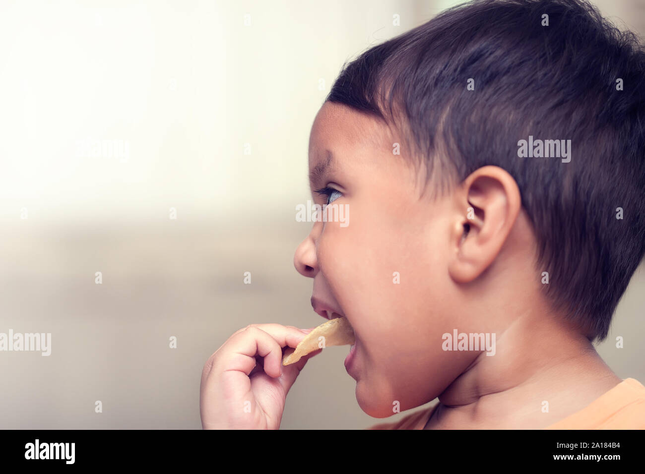 A kid forcibly putting a unhealthy potato chip snack in his mouth for eating while parents are away. Stock Photo