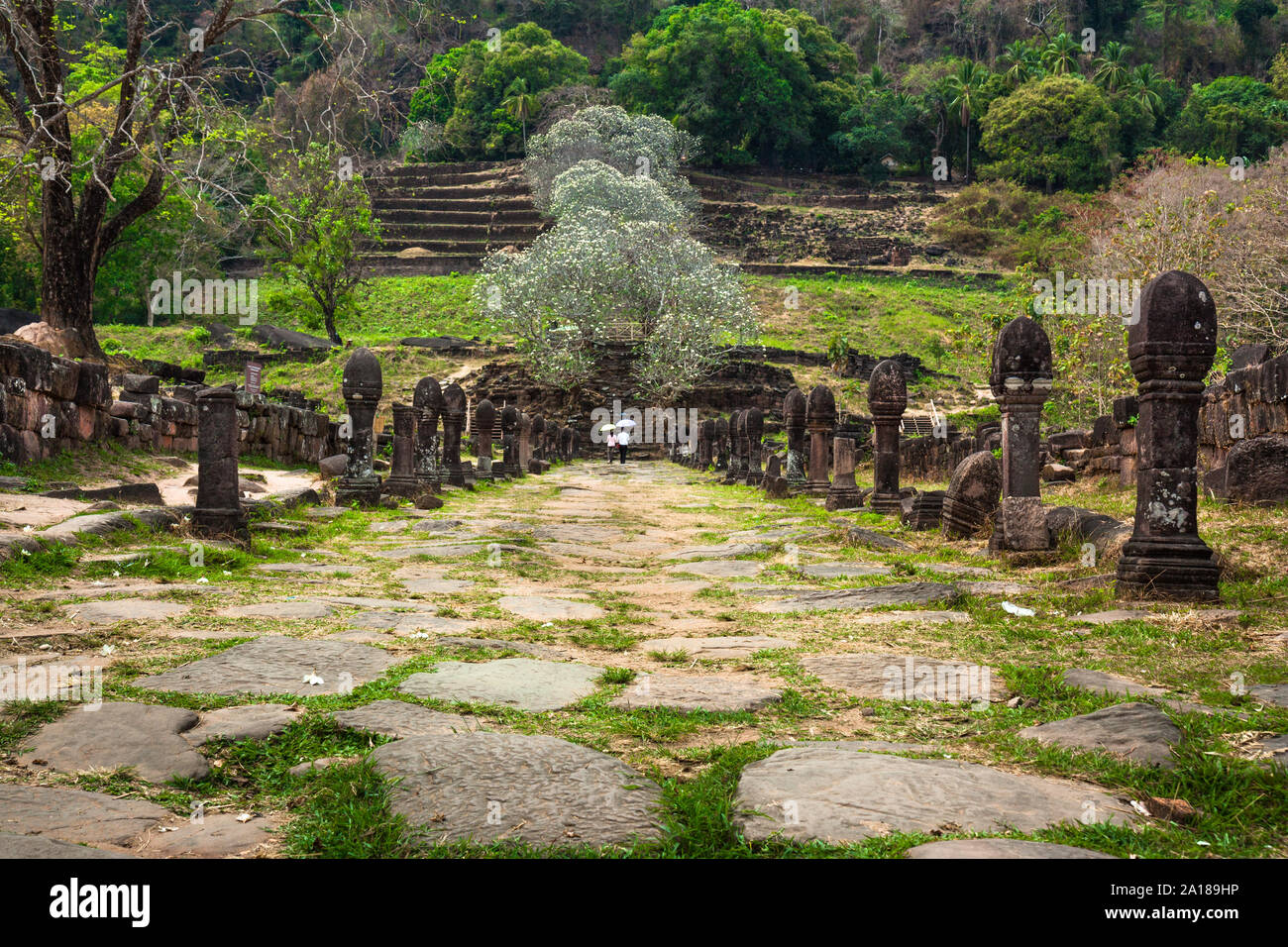 Two tourists in the entry pathway of Wat Phu, a pre-Angkor Khmer ruins, with Hindi then Buddhist temples. UNESCO WH Site. Champasak, Lao PDR Stock Photo