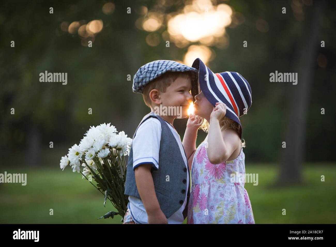 Little girl is kissing little boy on the cheek while he is hiding bouquet behind his back Stock Photo
