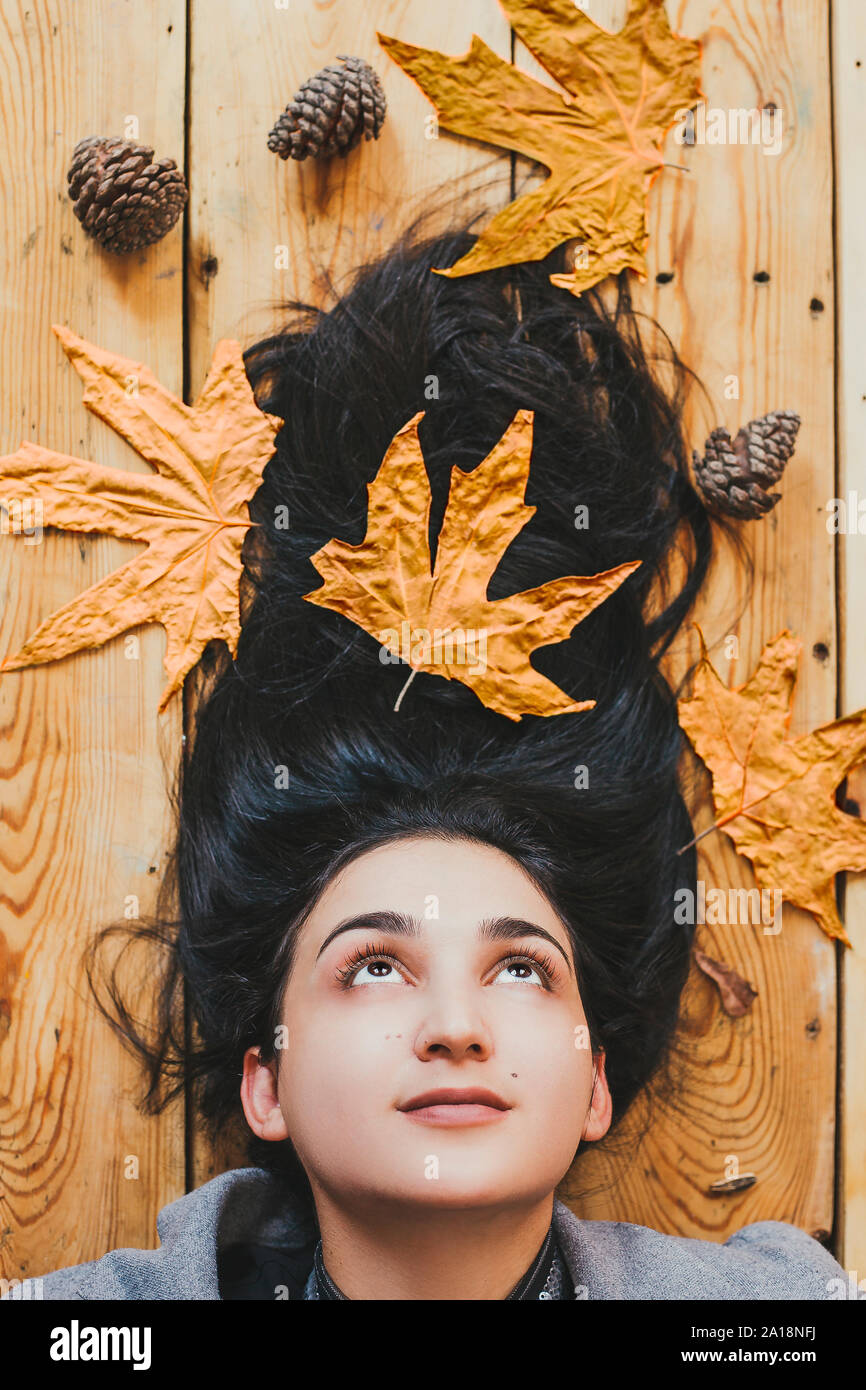 Autumn woman. Fall season concept. A portrait of lying on wooden floor woman. Young, beautiful and happy female holding a big yellow autumn leaf. View Stock Photo