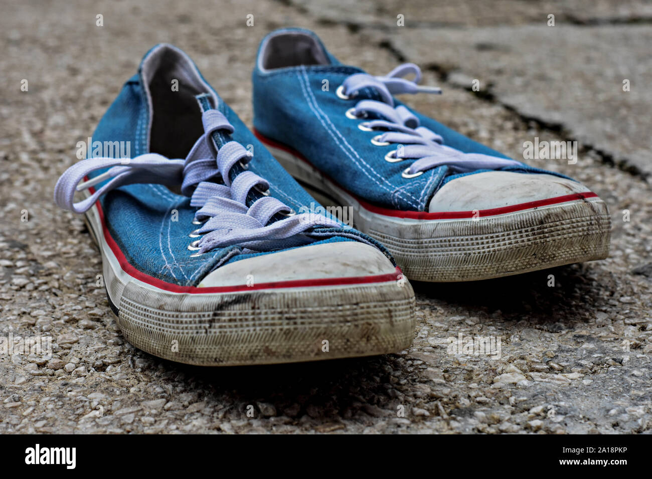 Old and shabby blue sneakers on concrete, asphalt road Stock Photo