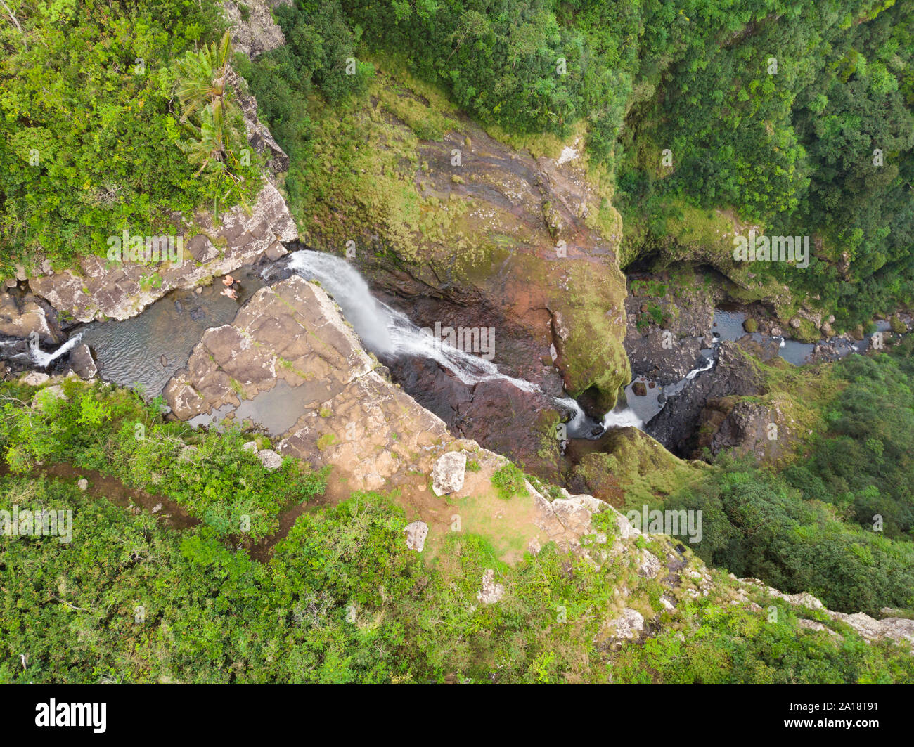 Aerial top view of travel couple waving to drone, standing on the edge of 500 feet waterfall in the tropical island jungle of Black river gorges Stock Photo