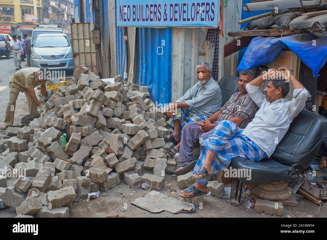 An employee at a construction site in Mumbai, India, sorting out bricks, watched by idling colleagues Stock Photo