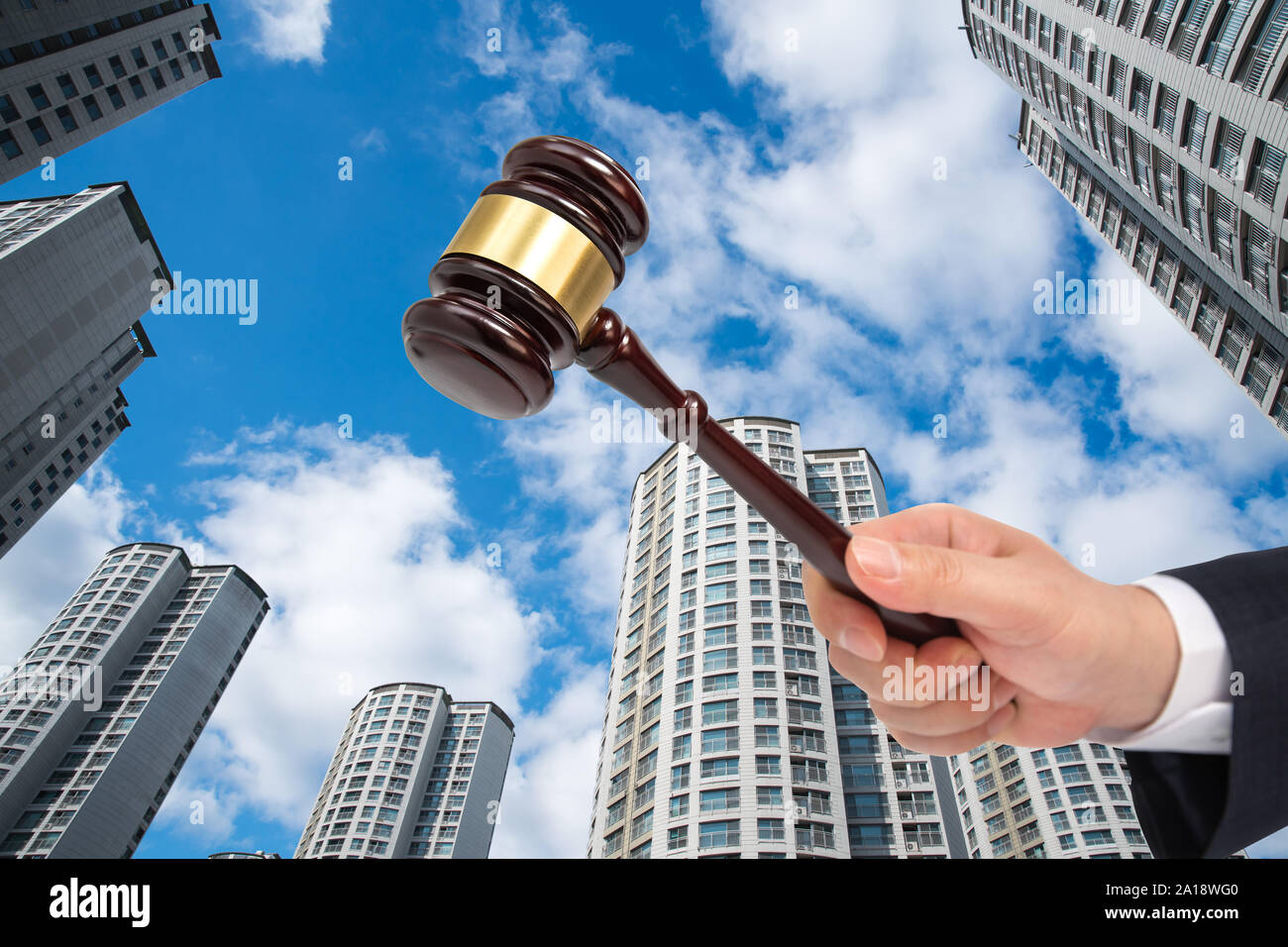 Hand of a businessman holding a judge gavel on the building background. Auction or bankruptcy concept. Stock Photo