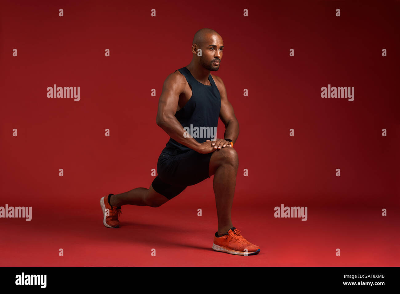Staying flexible. Handsome and strong african man in sports clothing stretching legs while standing against red background. Sport concept. Active and healthy lifestyle Stock Photo
