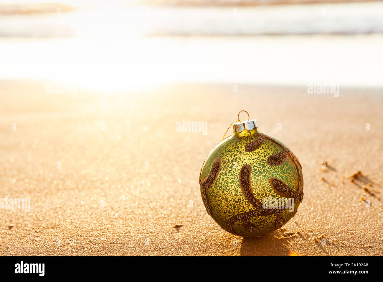 Green Christmas ball at golden sunset on the beach with copy space on