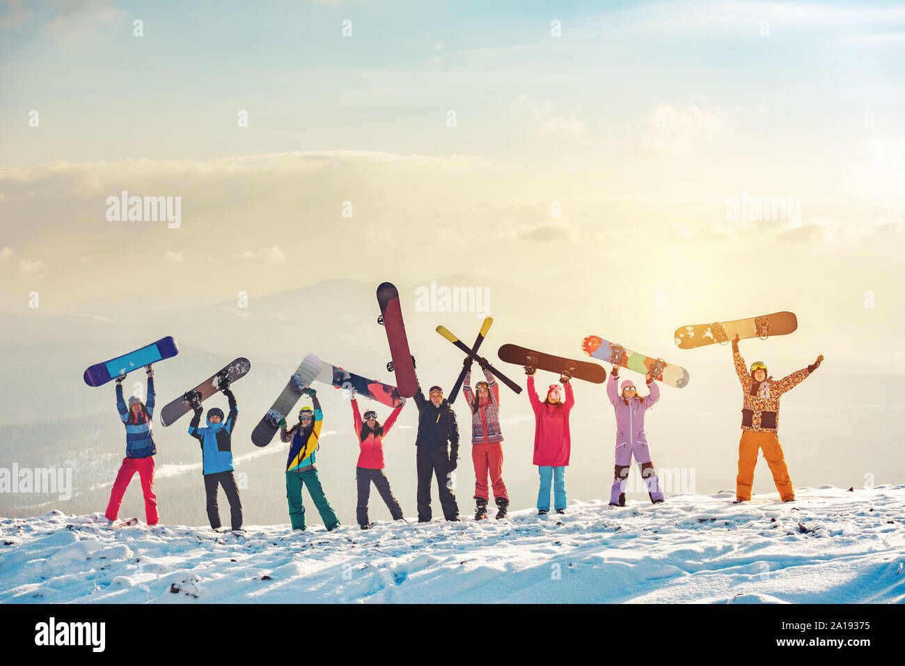 Big group of happy friends skiers and snowboarders having fun and holding ski and snowboards on mountain top Stock Photo