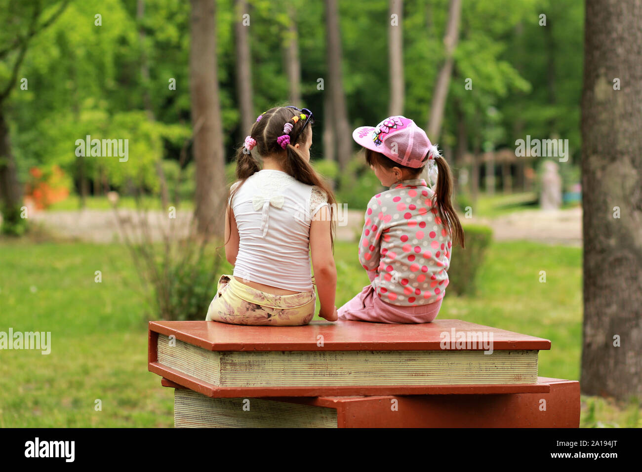 Two girls sitting on pile of giant books in the park, back view Stock Photo