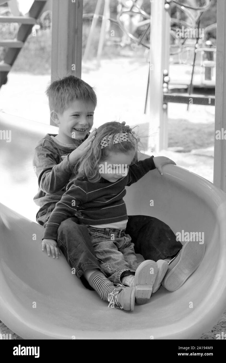Kids having fun because of hair raising static electricity on the plastic playground slide. Black and white portrait Stock Photo