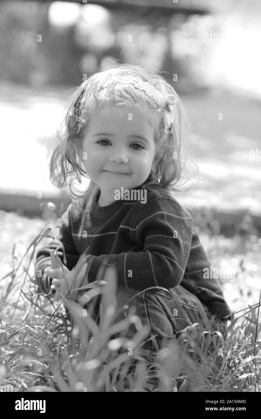 Black and white close up of extremely cute little one year old girl sitting in the grass outdoors Stock Photo