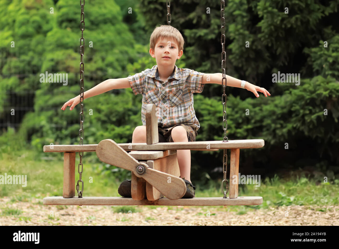 Five year old boy flying on a wooden plane swing in the summer park