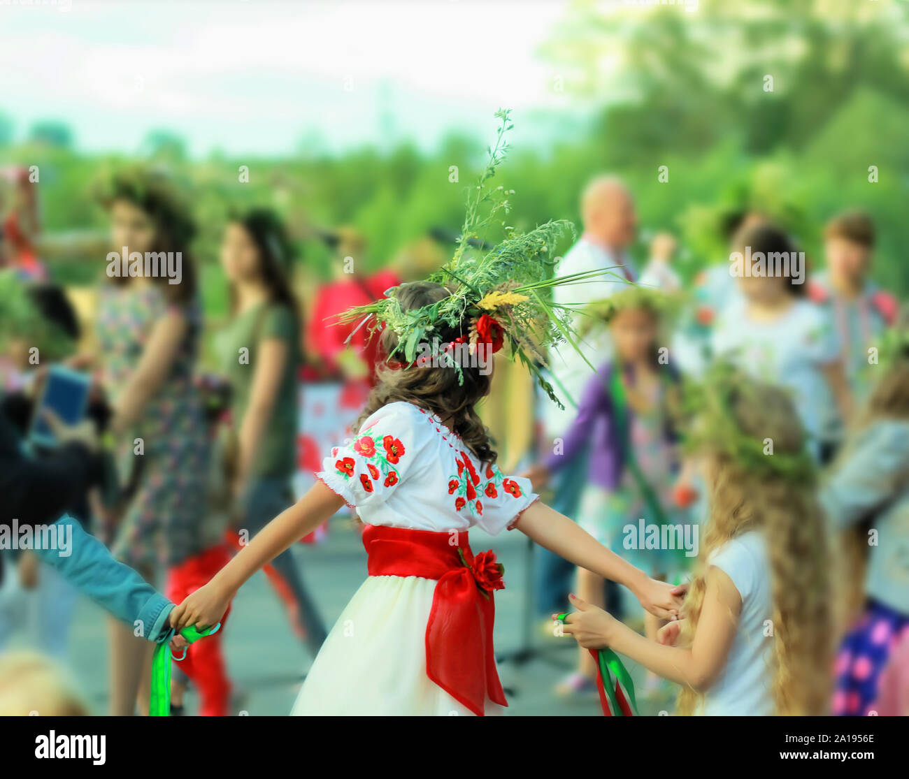 Young girl wearing a wreath and ethnic ukrainian clothes with embroidered red flowers dancing in a ring celebrating pagan holiday of Ivan Kupala Stock Photo