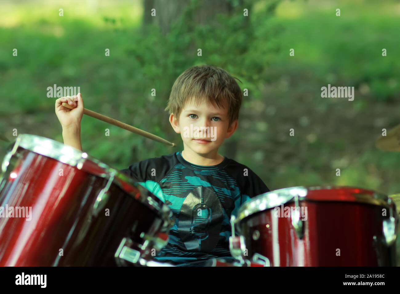 Five year old boy learning to drum outdoors in the park, close up