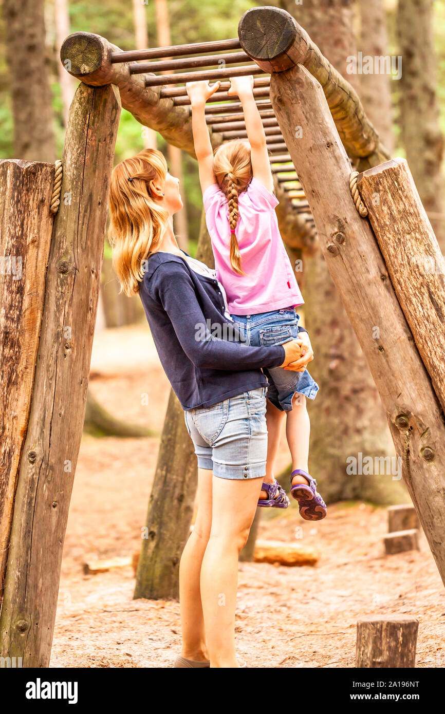 Mother Supporting daughter in the playground with climbing and hanging on a ladder. Stock Photo