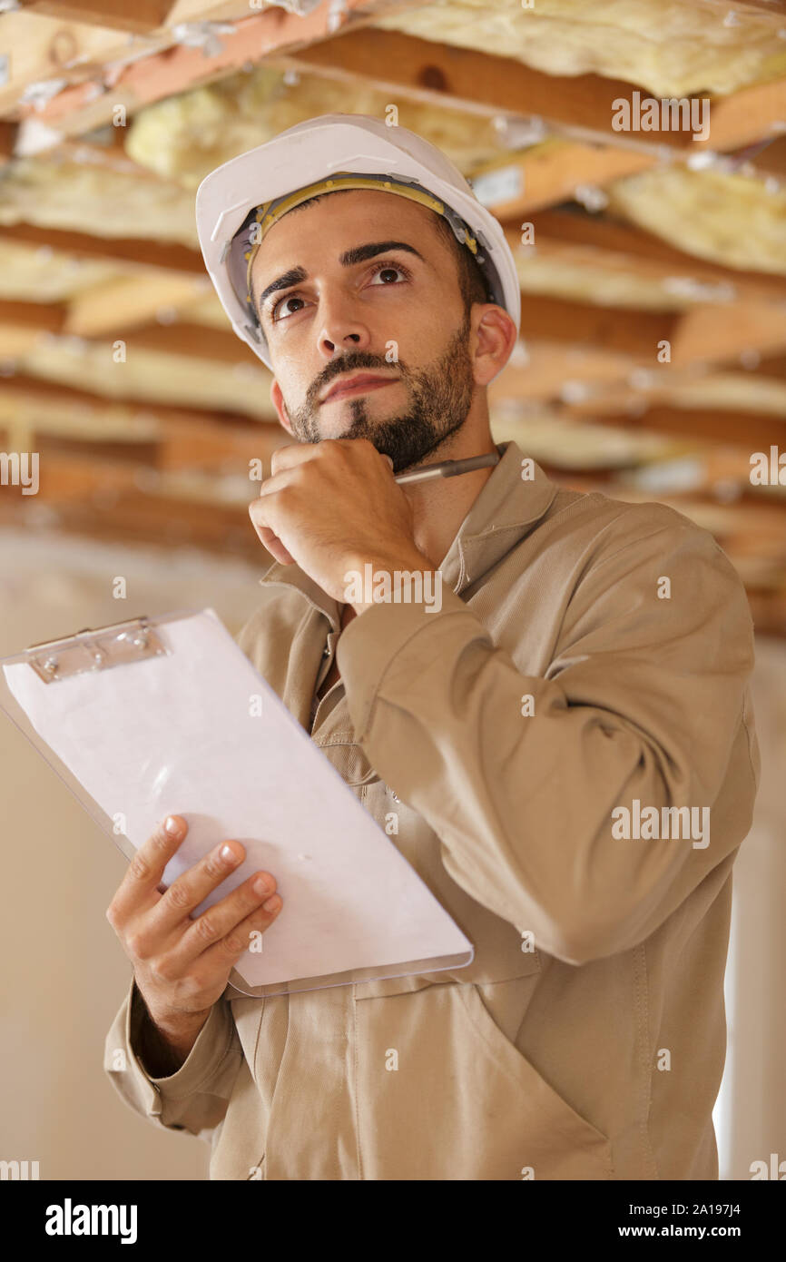young handsome builder thinking about something while holding clipboard Stock Photo