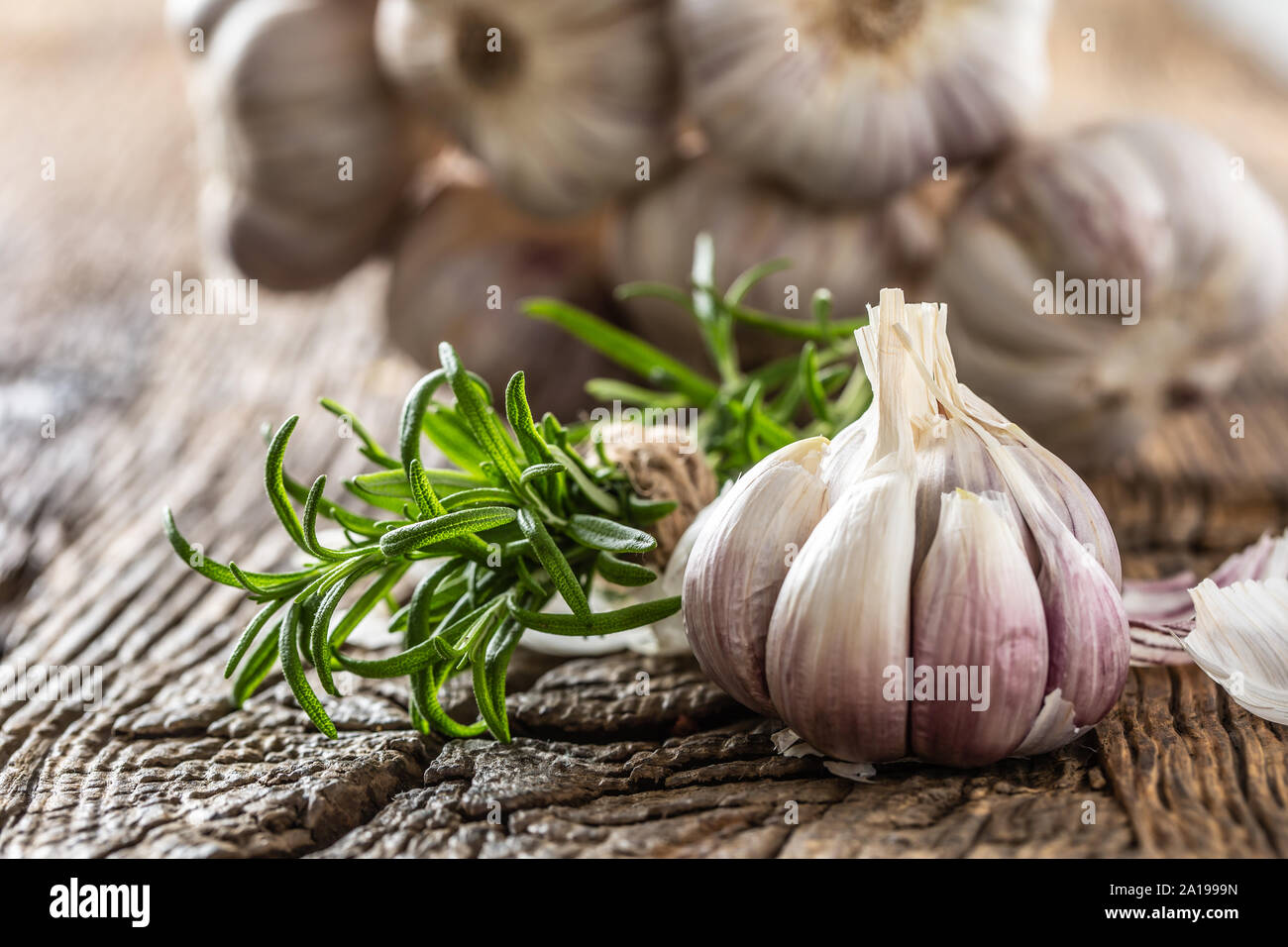 Garlic cloves and bulb with fresh rosemary on old wooden table Stock Photo