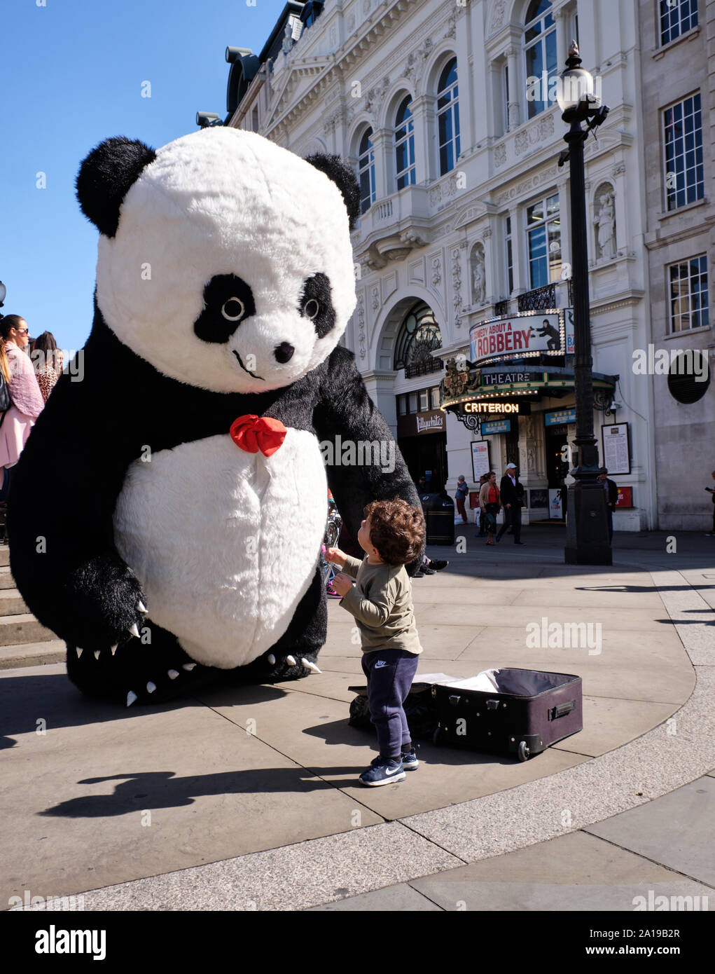 Small kid looking up at Street performer dressed in giant panda suit at Piccadilly circus Stock Photo