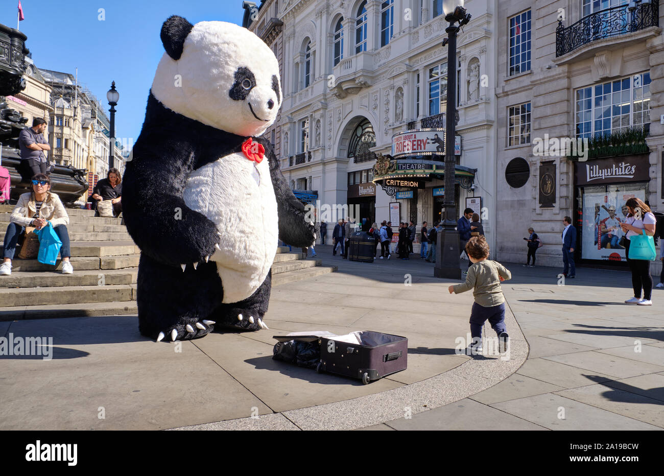 Street performer dressed in giant panda suit at Piccadilly circus with kid running around Stock Photo