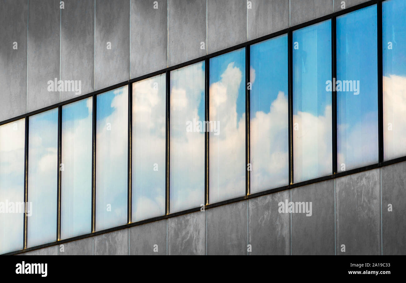 reflection of blue sky and white clouds in the windows of a gray ...