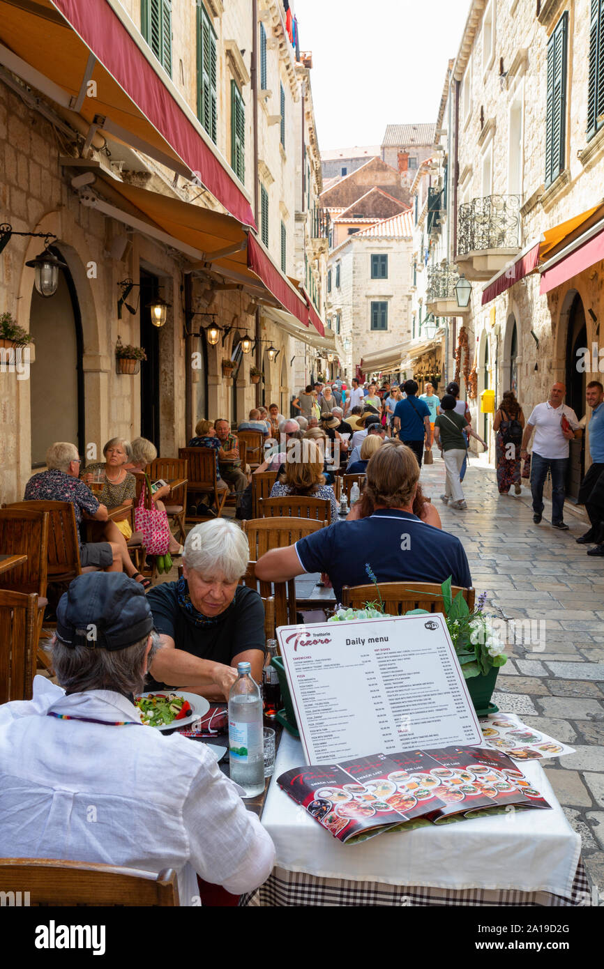 Dubrovnik Street restaurant - people eating at tables outside in a narrow street in daytime, Dubrovnik old town, Dubrovnik Croatia Europe Stock Photo