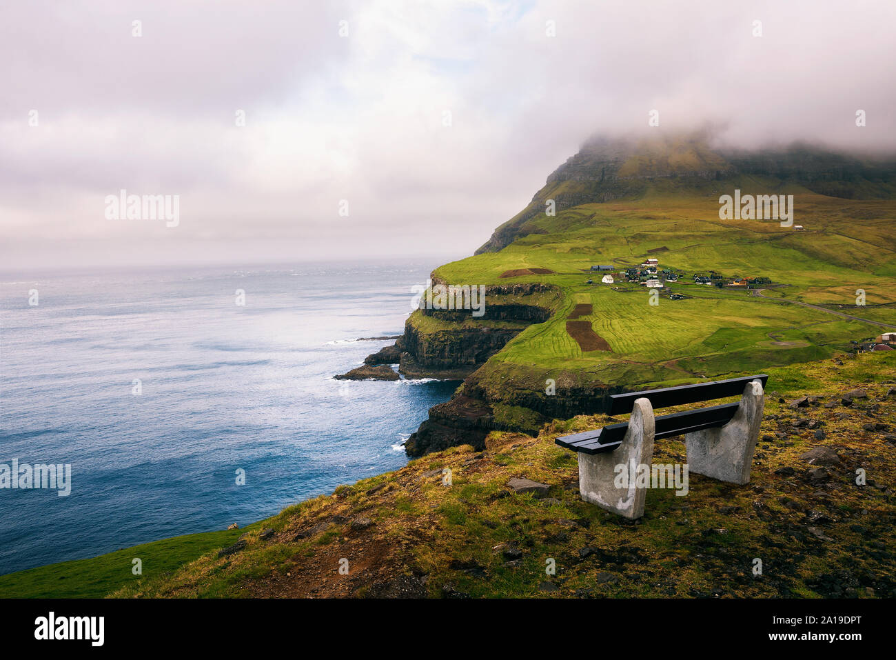 Bench above Gasadalur village with views over Atlantic Ocean on Faroe Islands Stock Photo