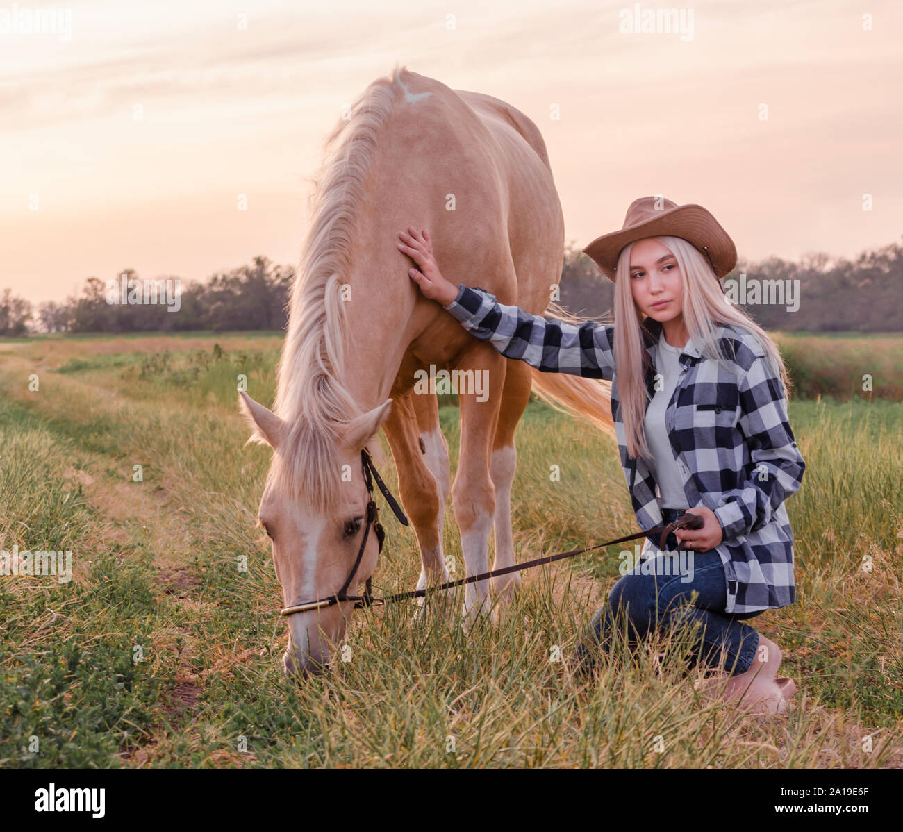 young blonde girl dressed in a cowboy hat and blue jeans with a horse at  the ranch Stock Photo - Alamy