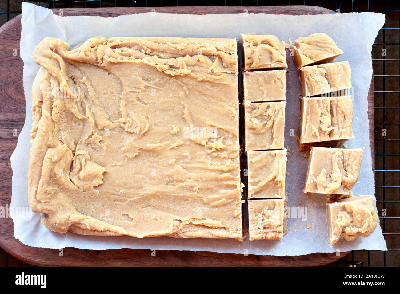 Whole block of delicious, homemade peanut butter fudge over a rustic wood cutting board being cut into squares. Stock Photo