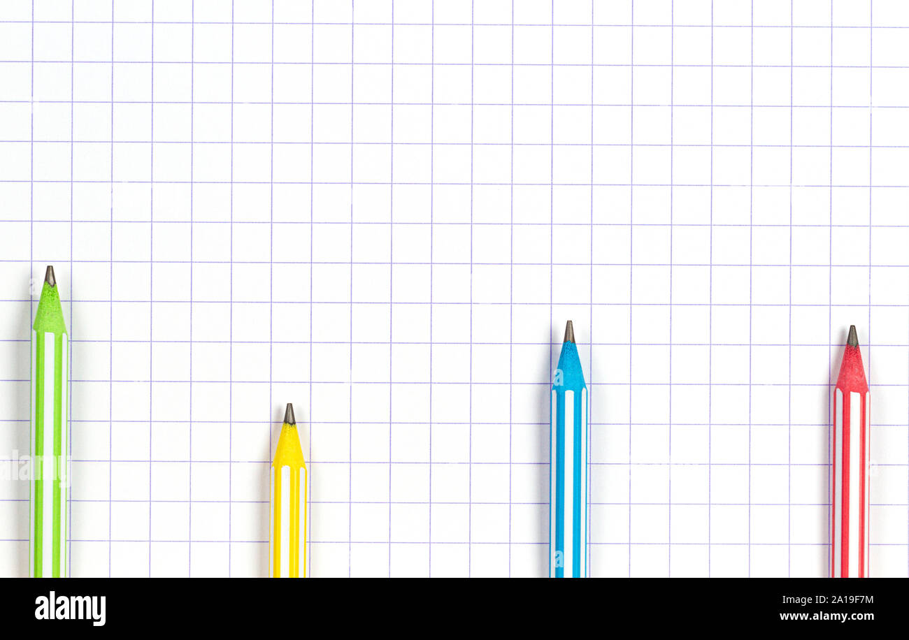 Multicolored striped pencils on white squared paper notebook background. Top view Stock Photo