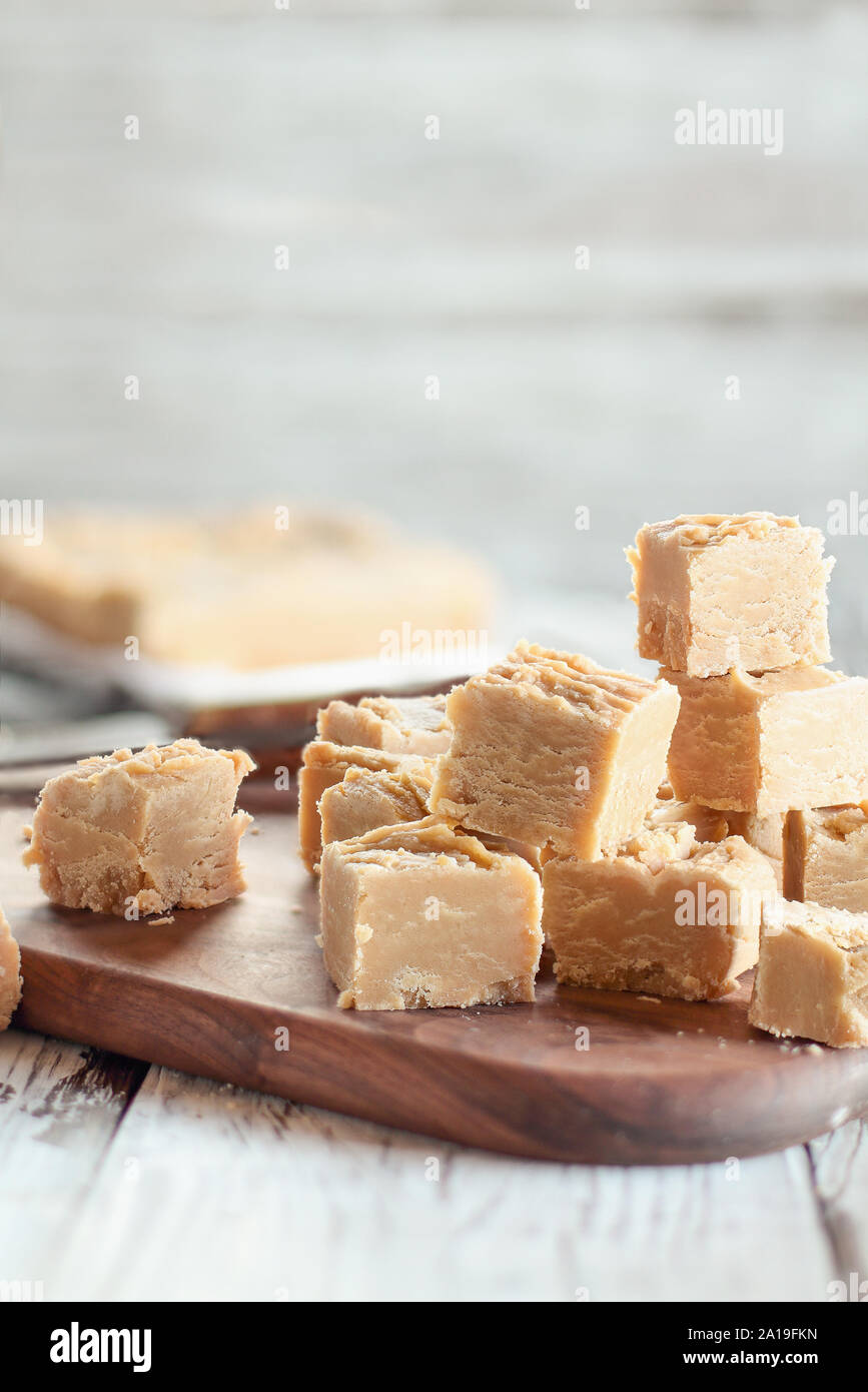 Squares of delicious, homemade peanut butter fudge over a rustic wood table. Selective focus on candy in the foreground with blurred background. Stock Photo