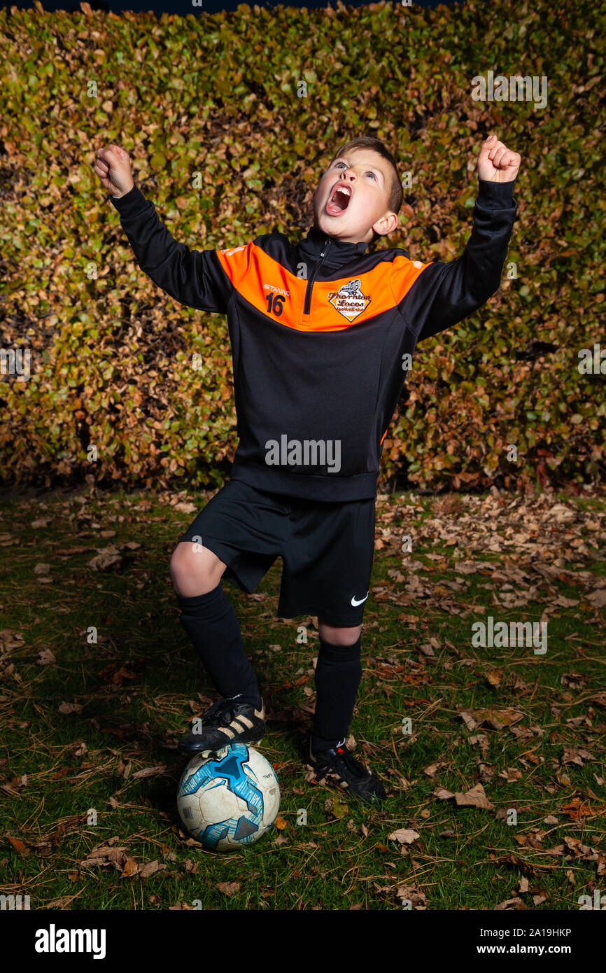 An eight year old boy wearing a football strip with arms raised and shouting. Stock Photo