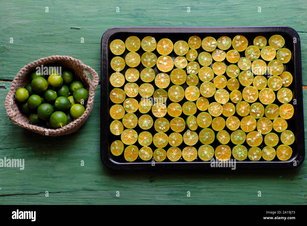 Top view black tray of many kumquat fruits cut in half with green peel and yellow flesh on green wooden background, this sour fruit rich vitamin c, he Stock Photo