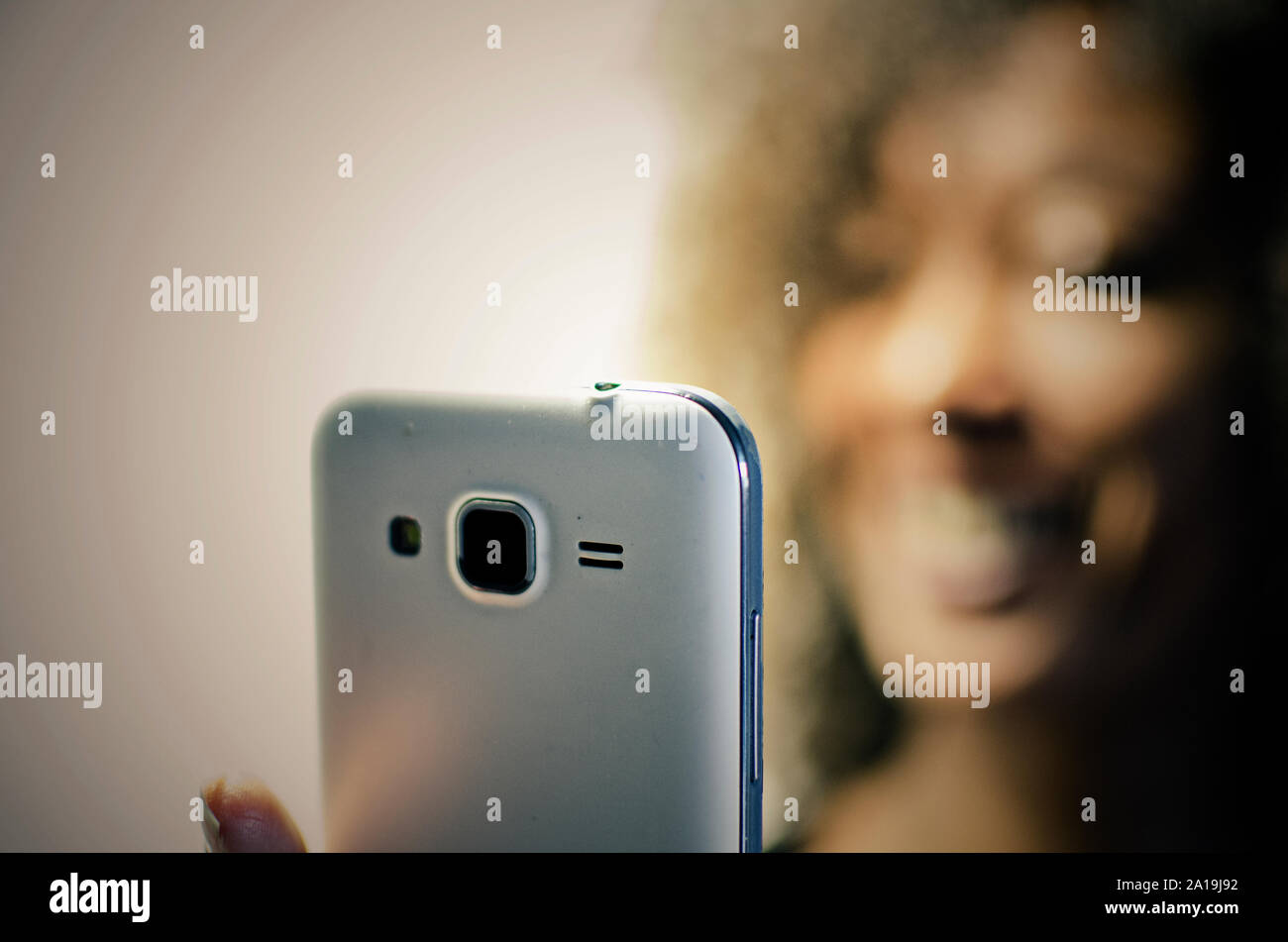 Smiling black woman looking at her phone. Selective focus on foreground. Blurred background. Stock Photo